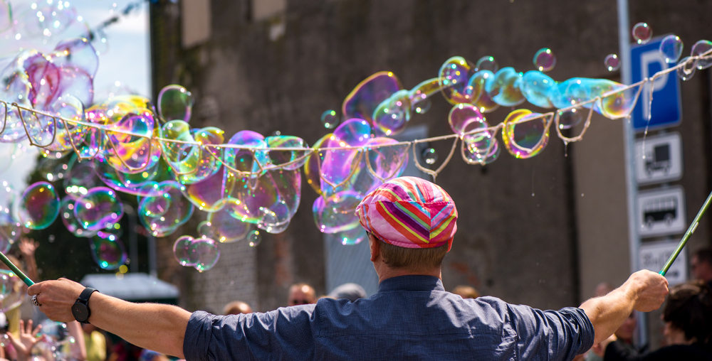 Man with a pink hat on, surrounded by large colourful bubbles on a string.
